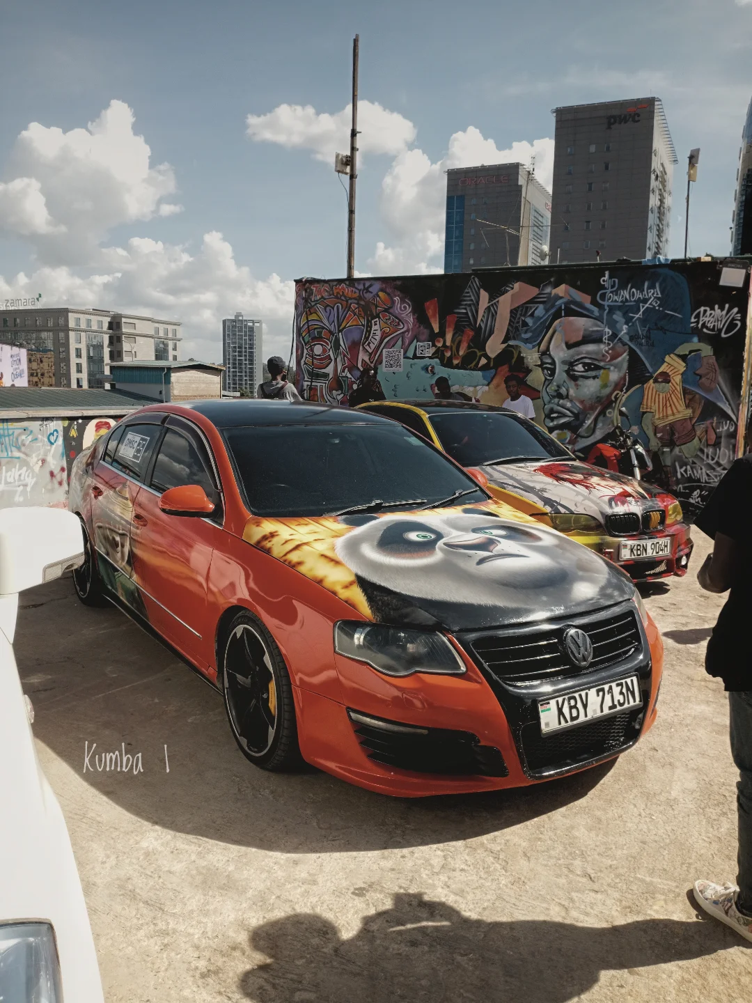 Orange custom VW at a car show in front of a graffiti wall